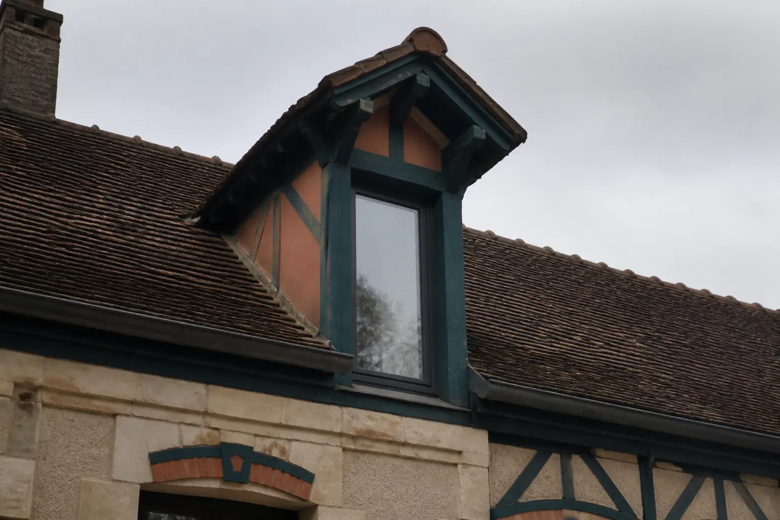 Toiture chien assis sur vieux toit résidentiel, lucarne à fenêtre verticale et charpente apparente.