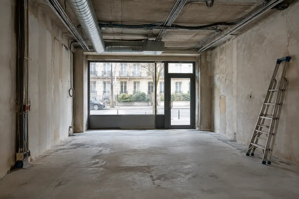 Intérieur brut d'un local commercial vide, sol en béton et gaines au plafond